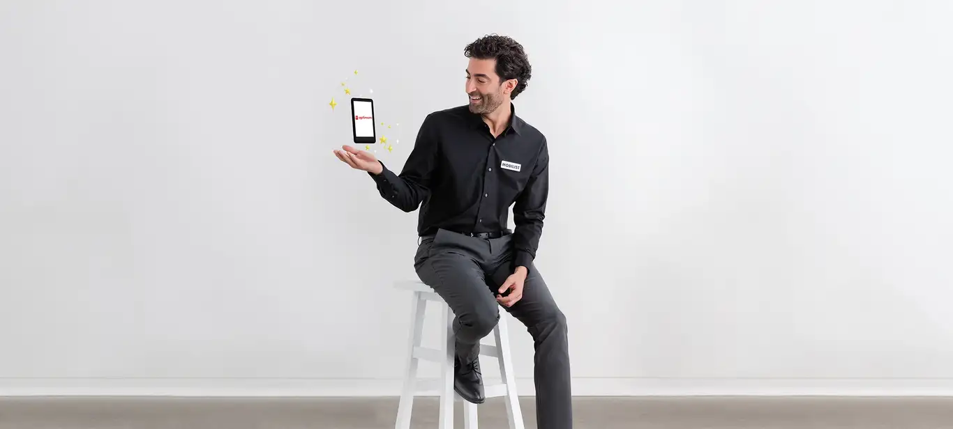 PC Optimum shows on the phone hovering over the hand of a Mobilist man perching on a white chair